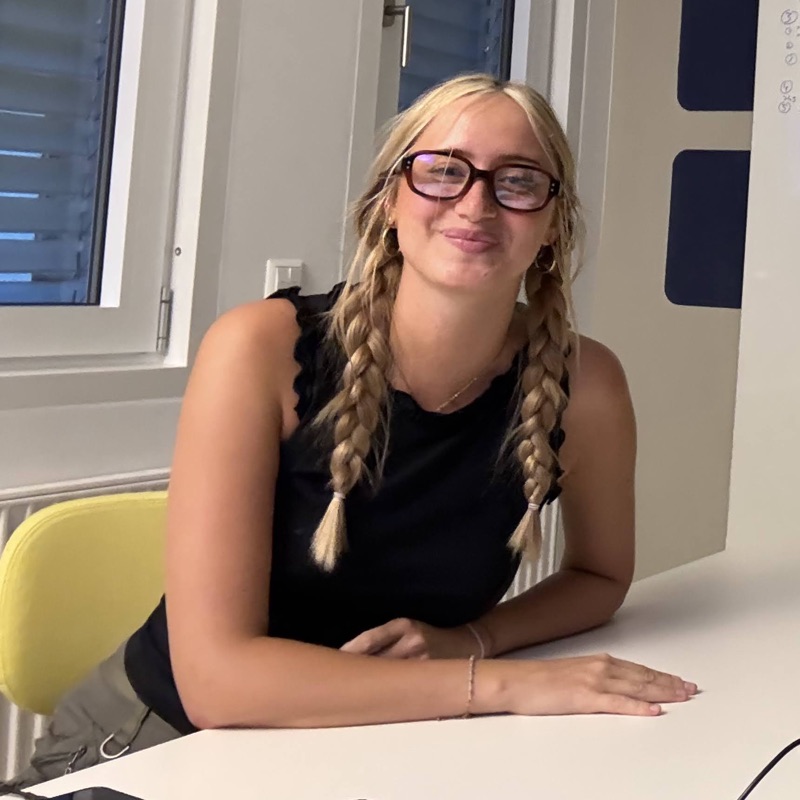 Leah mit Brille und geflochtenen Zöpfen an einem Tisch