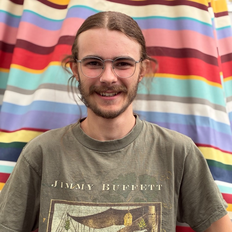 Max mit Brille vor einem bunt gestreiften Vorhang